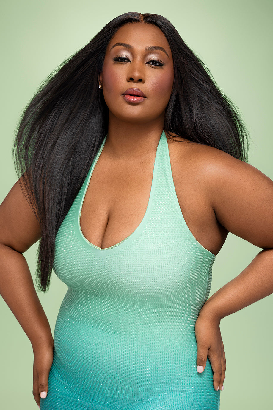 A confident person with long hair wearing a light teal halter dress.