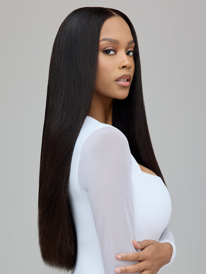A woman with long, straight, dark brown to black hair wearing a white long-sleeve top, shown from the side against a solid gray background.