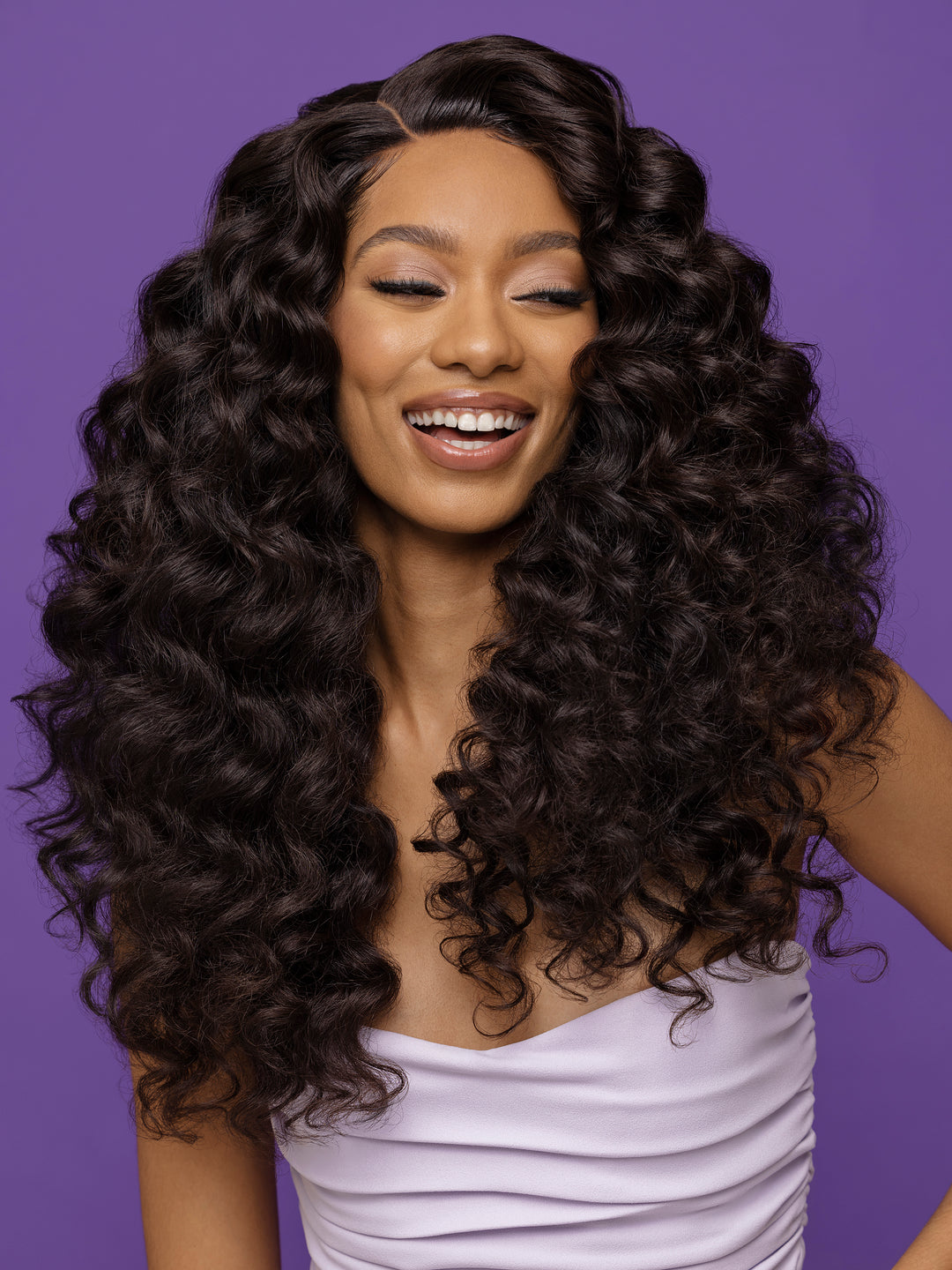 Woman with long, curly hair smiling against a purple background