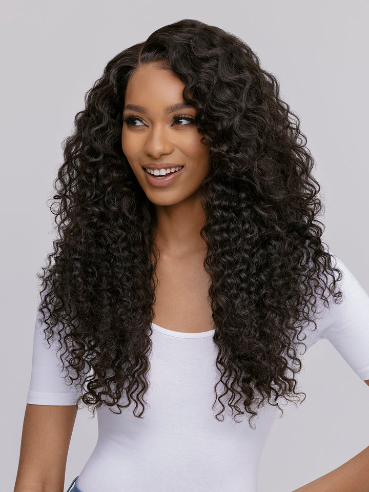 Woman with long, curly hair wearing a white top against a plain background